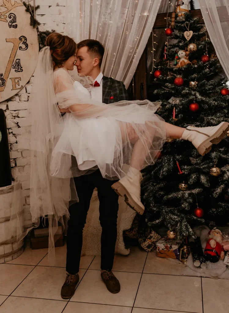 A groom holding his bride in front of a Christmas tree.