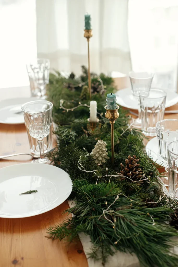 A beautiful table arrangement featuring a garland, candles and pinecones.