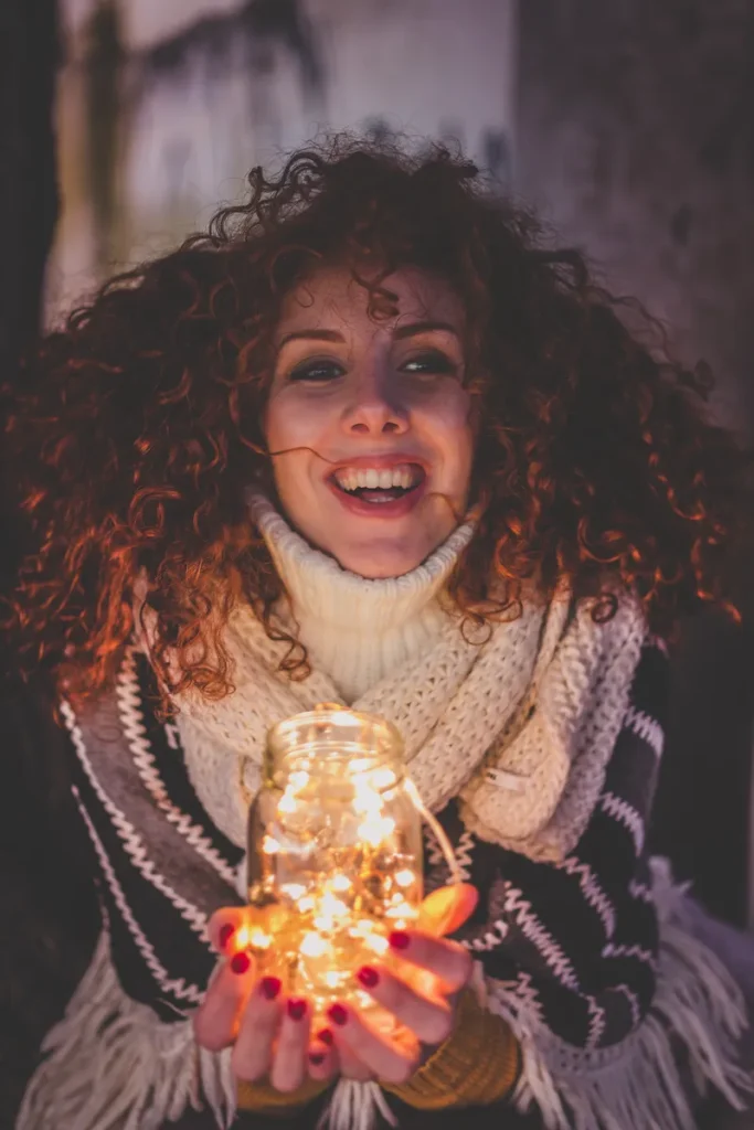 A woman holding a mason jar full of fairy lights instead of a candle.