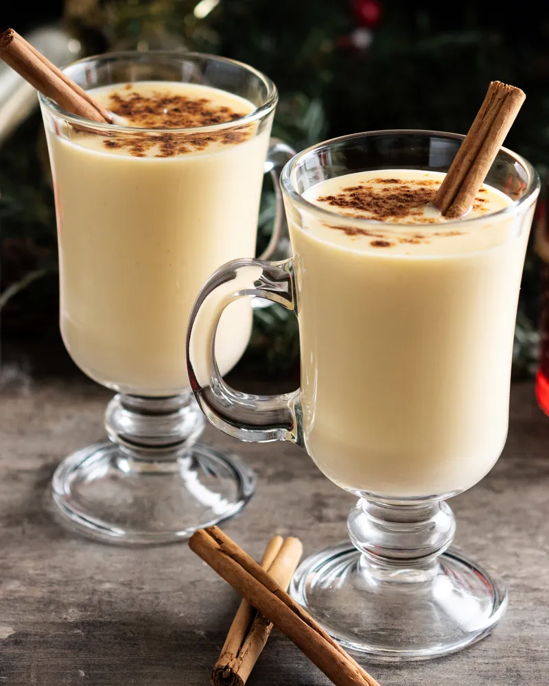 Eggnog served with some cinnamon sticks in glass mugs.