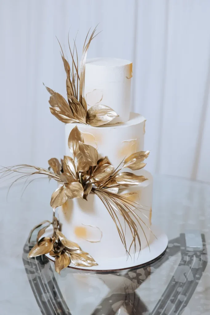 A white cake accented with gold smears and gold leafed foliage.