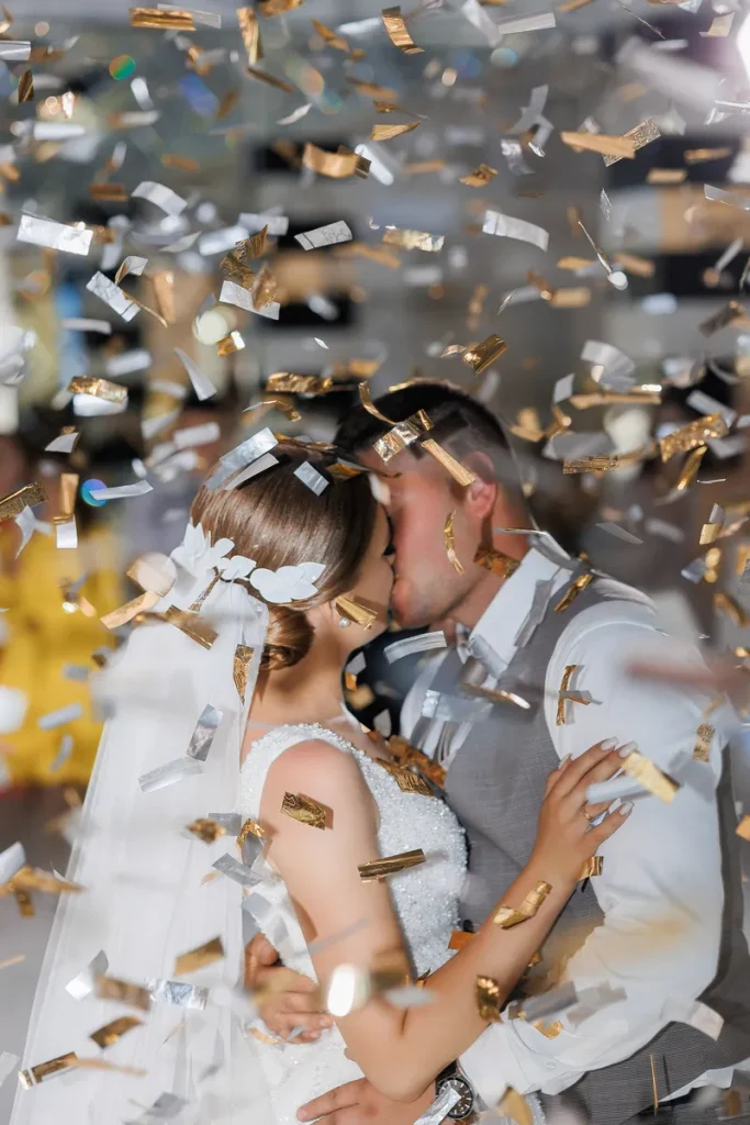 A bride and groom having a kiss as metallic confetti falls around them.