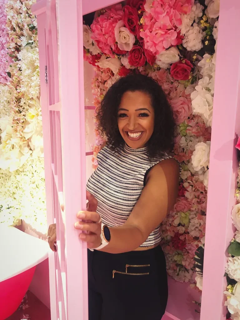 A woman coming out of a flower filled photobooth.