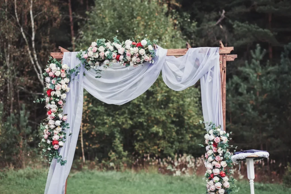 A wooden arbor draped with gauzy fabric and floral garlands.