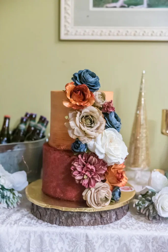 A rustic boho wedding cake with orangey icing in an ombre and dried flowers trailing down the side.