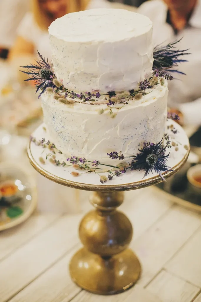 A rustic boho wedding cake with textured buttercream, dried flowers ringing the layers.