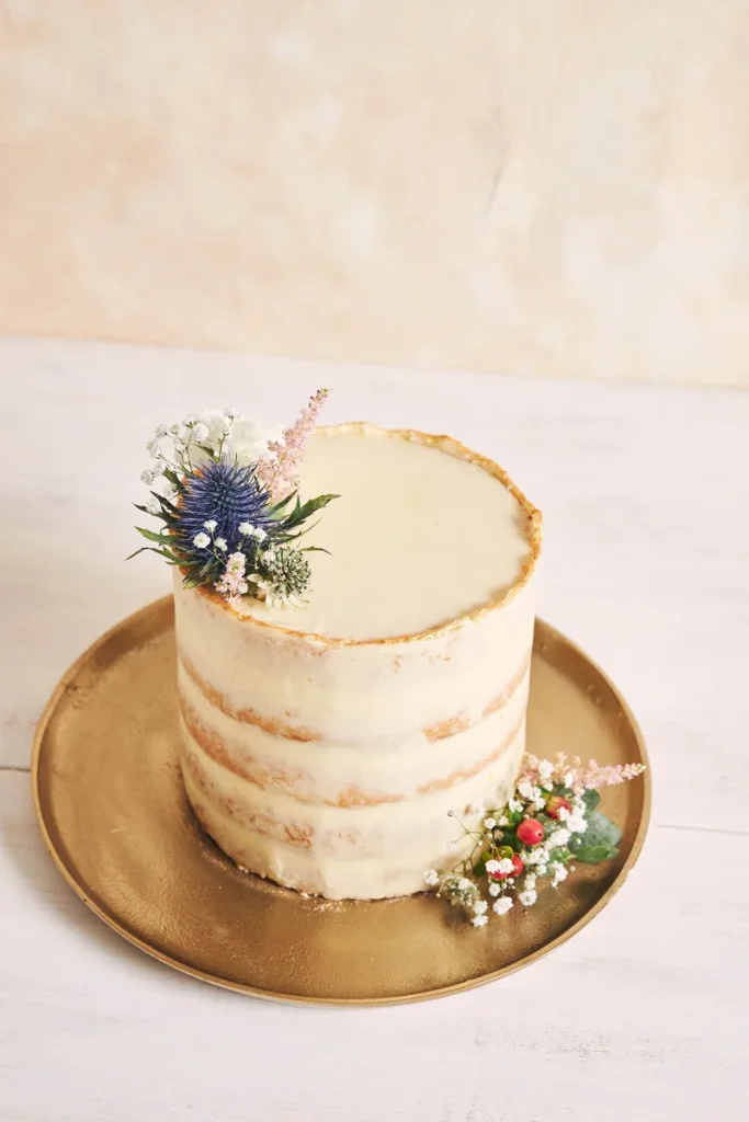 A rustic naked wedding cake, with some flower details.