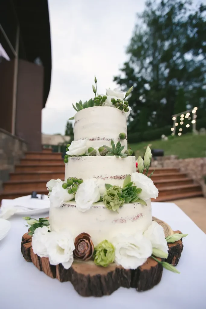 A rustic naked wedding cake with some green flowers and succulents decorating the tiers.
