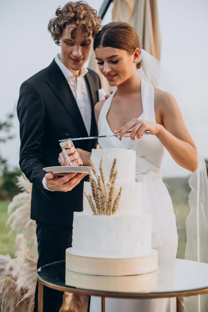 A simple rustic wedding cake with white textured frosting and a simple dried wheat frond on front.