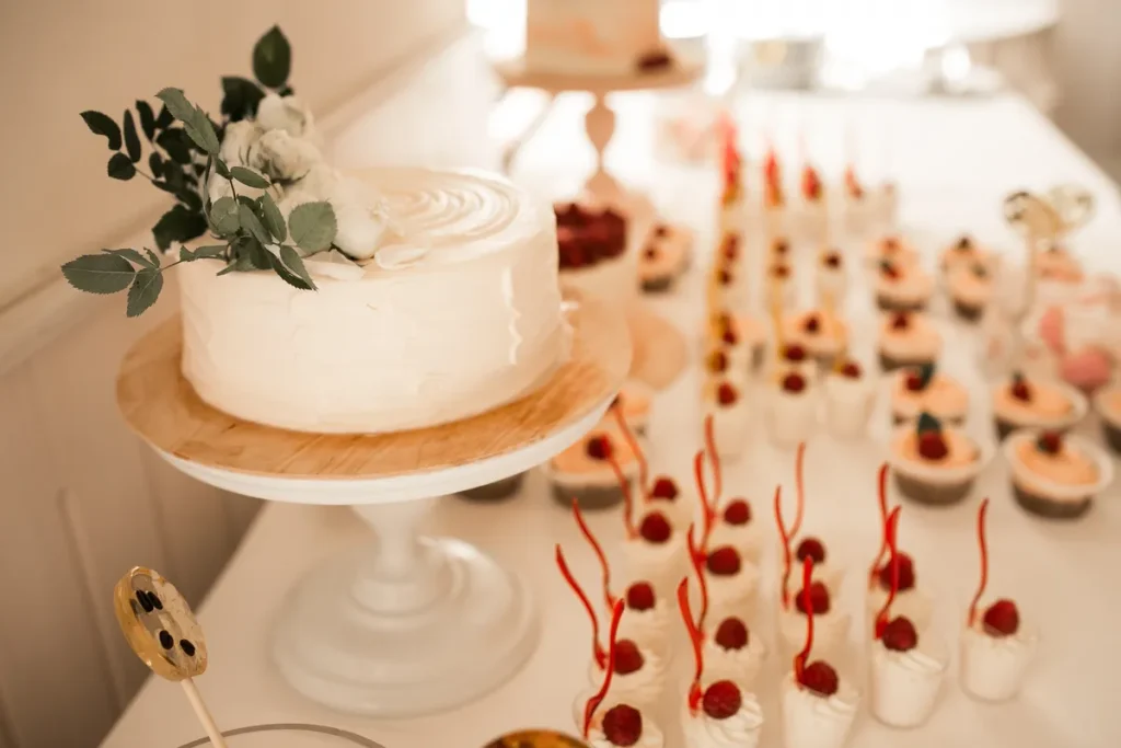 A small rustic wedding cake with simple icing but a lot of other sweets to accompany it.