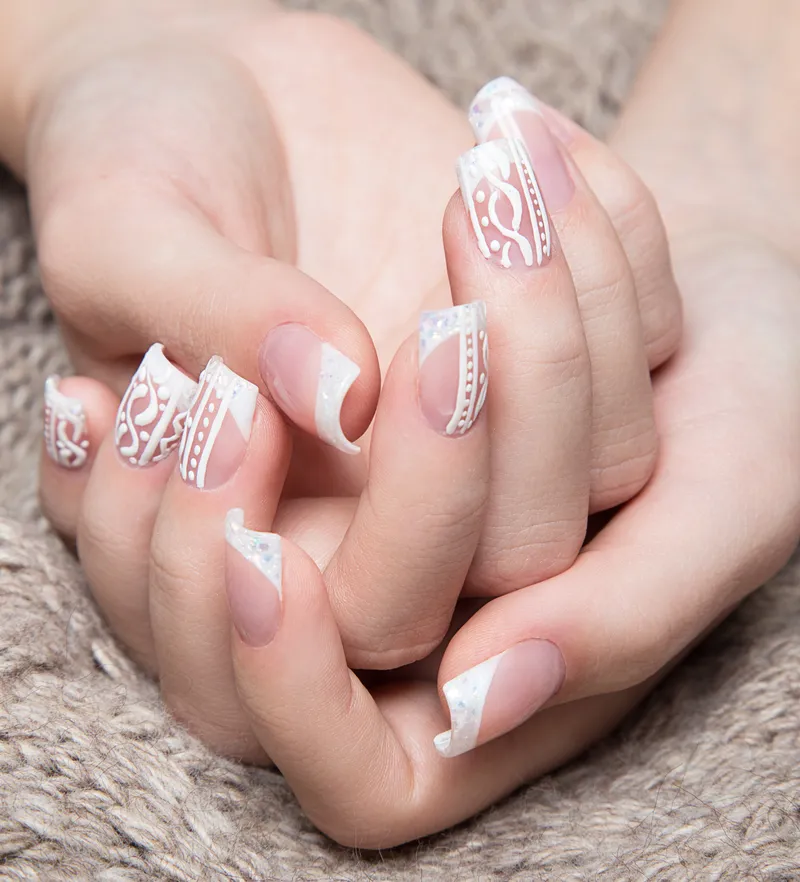 A french tip manicure with lace detailing over the nail.