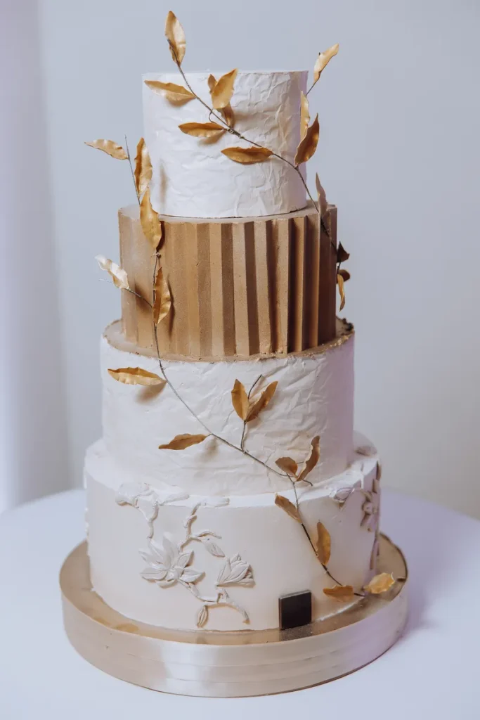 A multi-tiered fall wedding cake with some gold leaves decorating it.