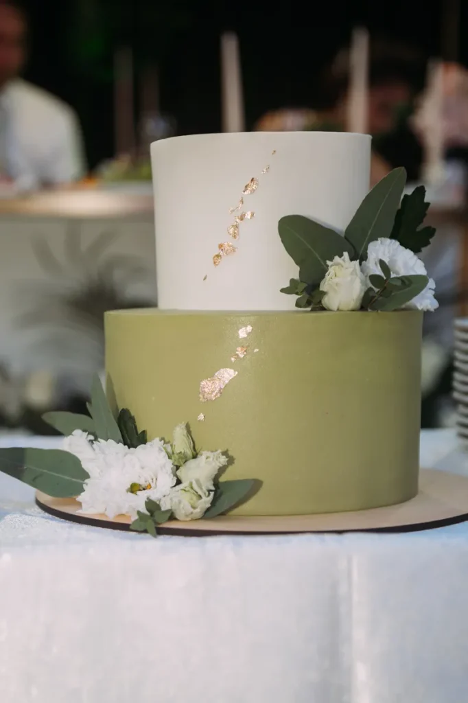 A sage green fall wedding cake with some simple greenery and flowers and a little gold leaf.