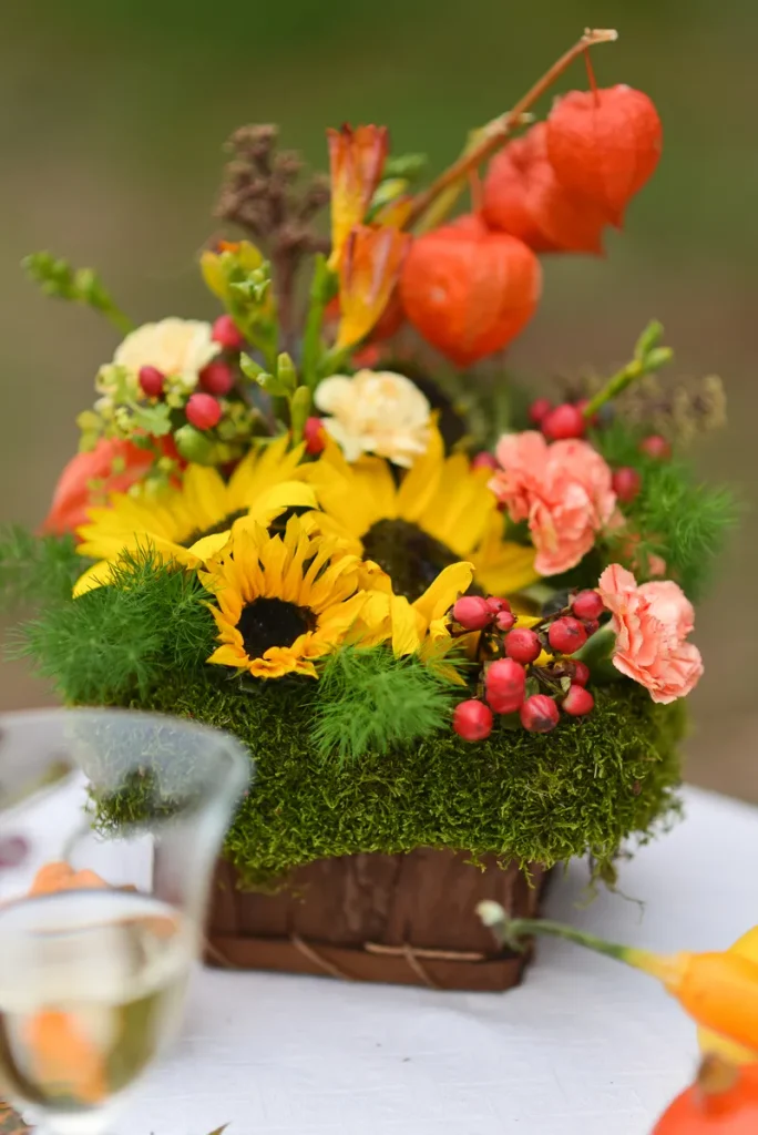 A rustic fall wedding centerpiece featuring sunflowers, moss and lantern flowers.